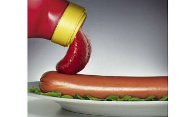 Fotografía de primer plano de ketchup cayendo sobre un perrito caliente