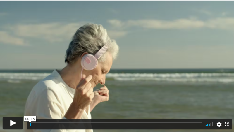 Una mujer mayor escuchando música, bailando y cantando mientras pasea por la playa.