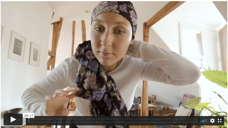 Una mujer con cáncer, se coloca un pañuelo.