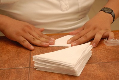 Unas manos doblando servilletas de papel en forma triangular