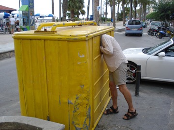 Imagen de una persona con la cabeza dentro de un contenedor y un coche descapotable detrás