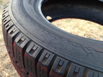 Imagen parcial de un neumático usado apoyado sobre un suelo de hierba seca