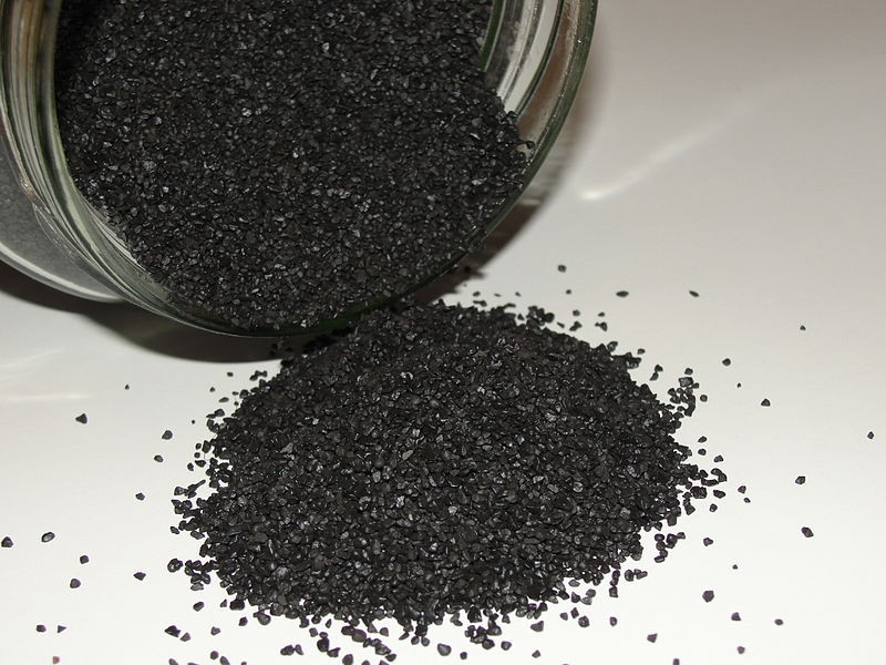 Material granulado de color negro contenido en un tarro de cristal y volcado en una superficie blanca