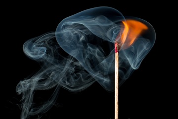 Cerilla encendida desprendiendo una llama y humo sobre un fondo negro
