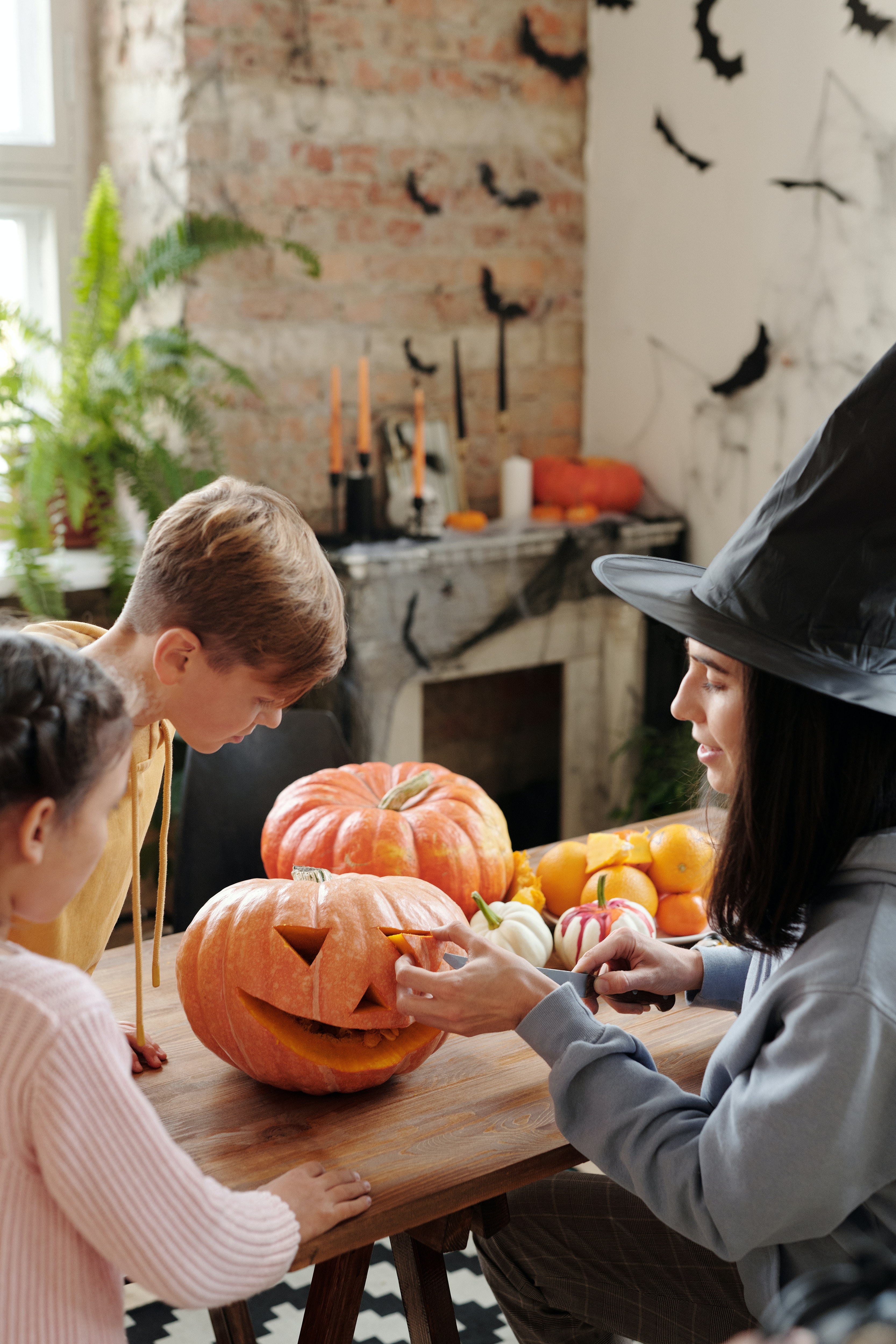 Imagen que muestra a una madre decorando una calabaza, con su hija y su hijo, para Halloween.