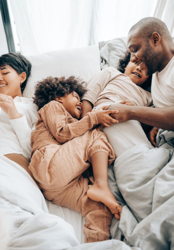 Fotografía de una familia jugando en la cama a hacerse cosquillas.