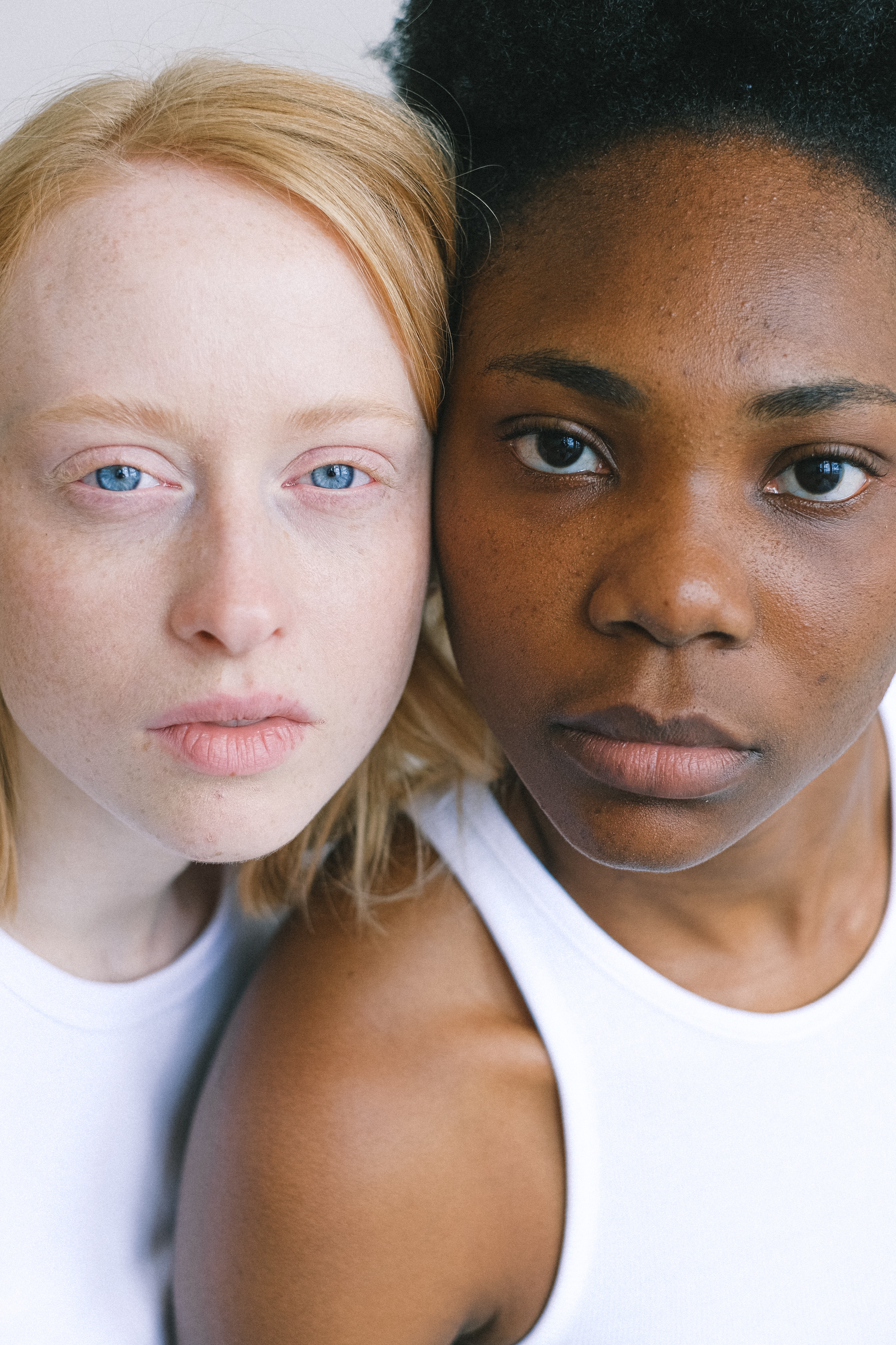 Mujer blanca rubia y de ojos azules y a su lado una mujer negra de ojos y pelo oscuro