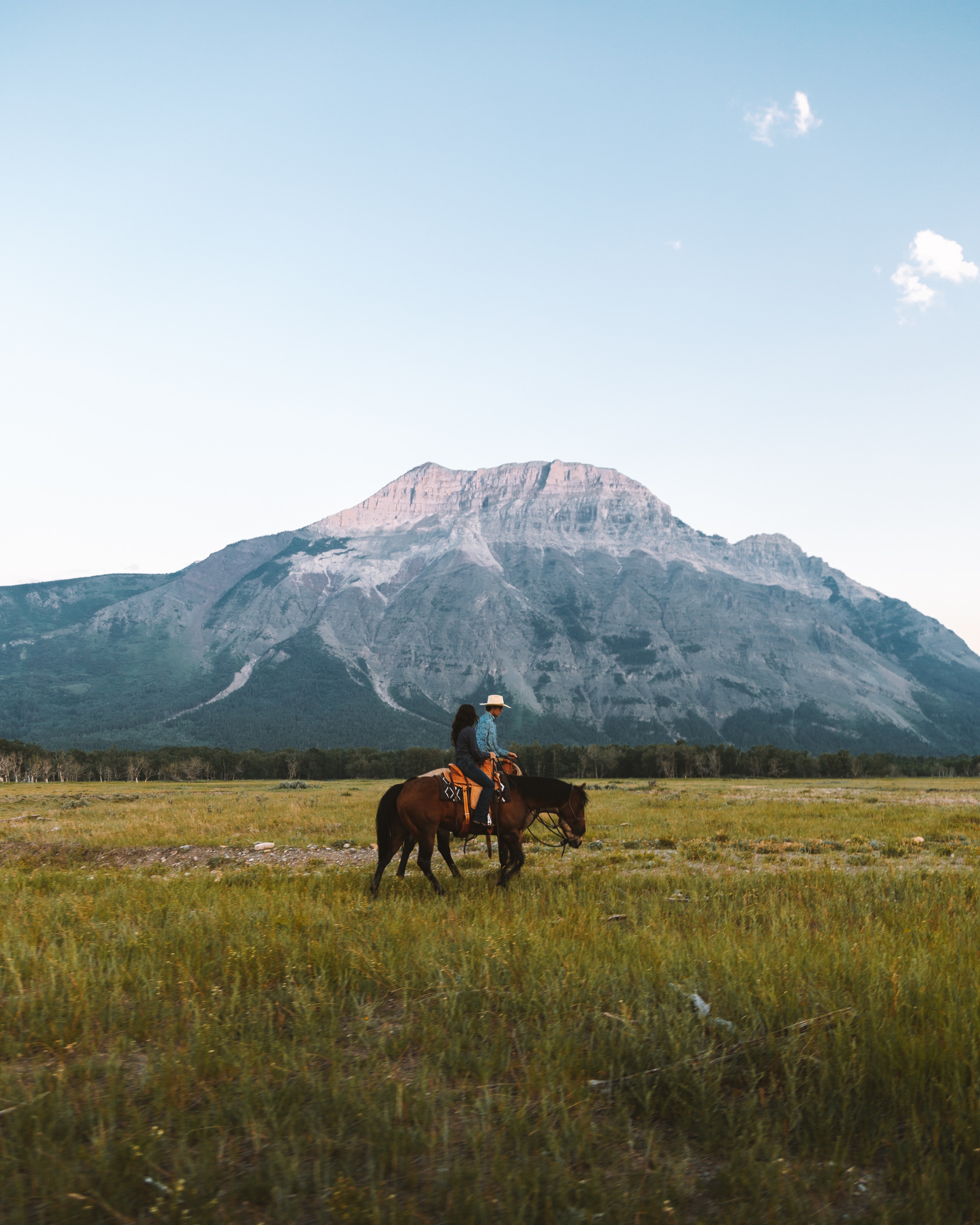 Un hombre y una mujer montando a caballo en el campo con una montaña detrás.