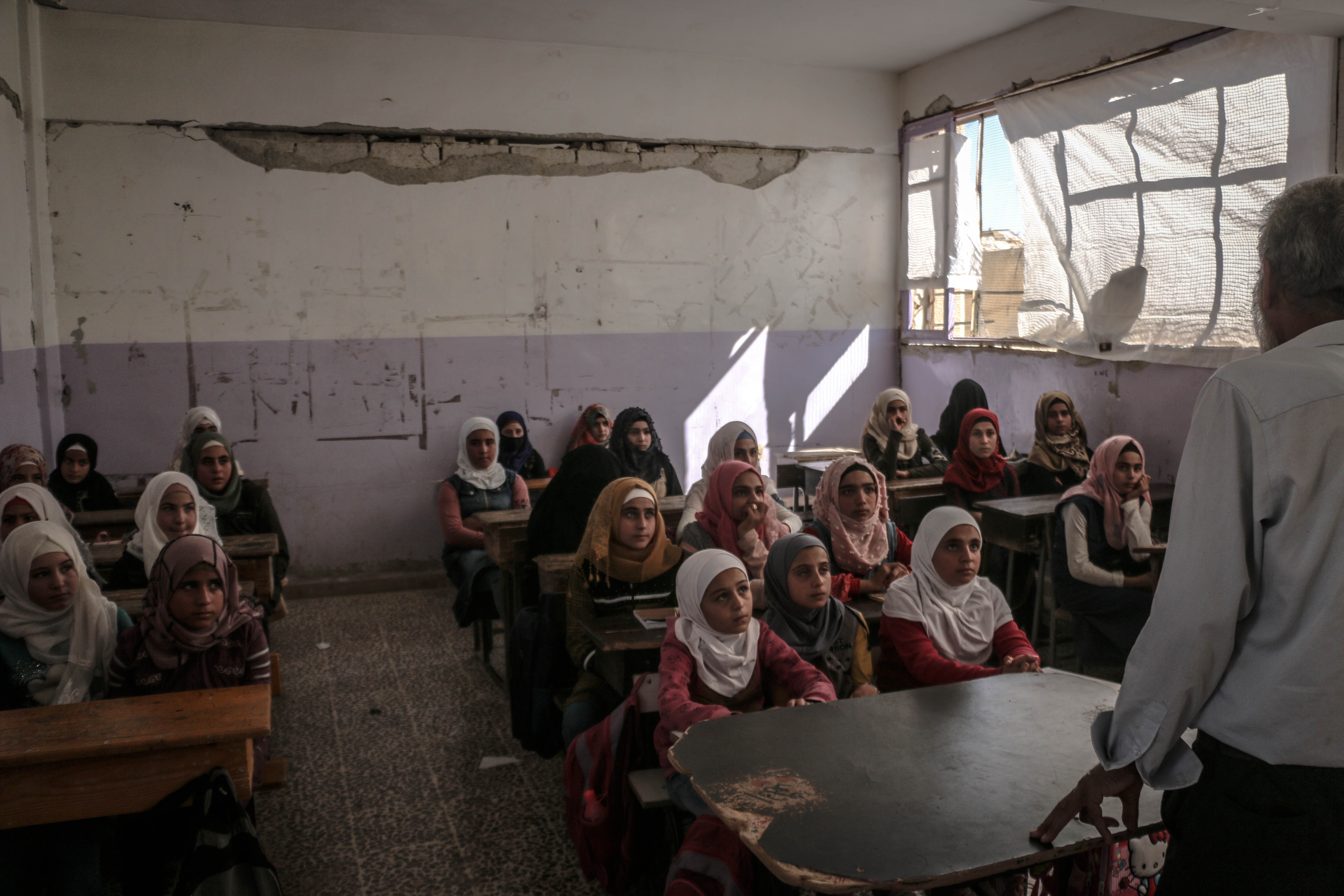 La imagen muestra un grupo de alumnas en una clase en ruinas.