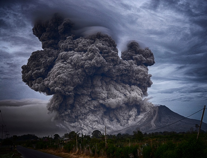 La imagen muestra un volcán en erupción cerca de una carretera.