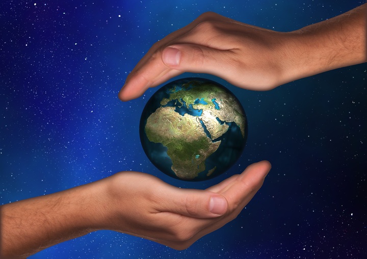 La imagen muestra dos manos haciendo como que sostienen al planeta Tierra, con la imagen de un cielo azul estrellado detrás a modo de fondo.