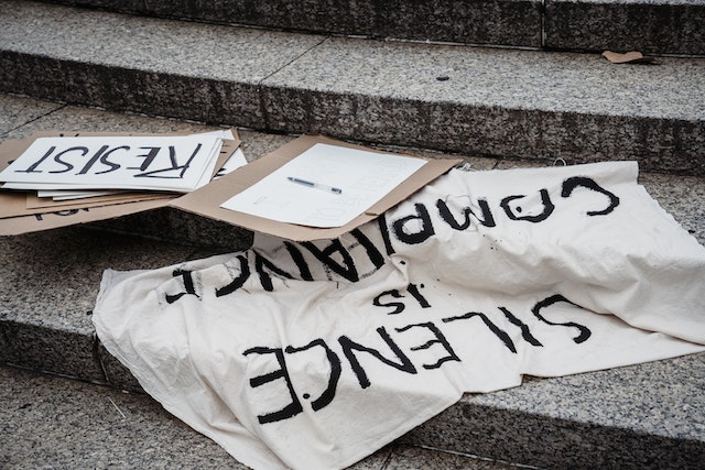 La imagen muestra varios carteles con slogans solidarios en una escalera junto con papel y bolígrafo.