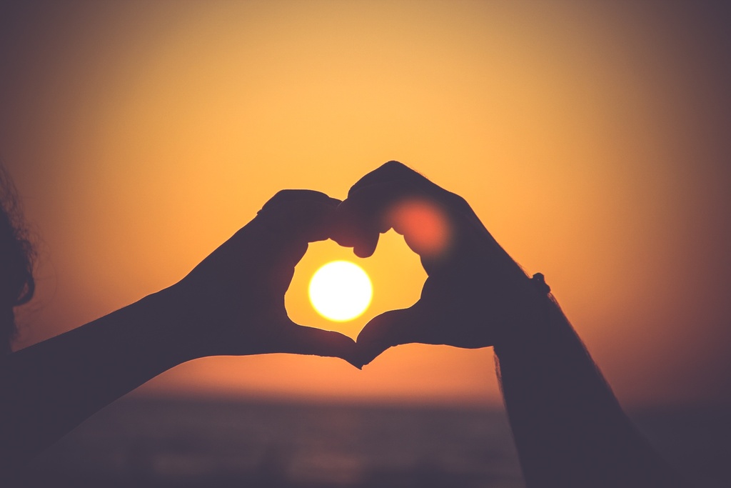La imagen muestra dos manos formando un corazón delante de una puesta de sol.
