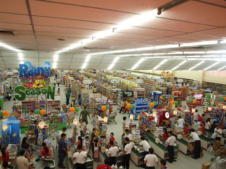 La imagen muestra una vista aérea del interior de un supermercado lleno de gente.