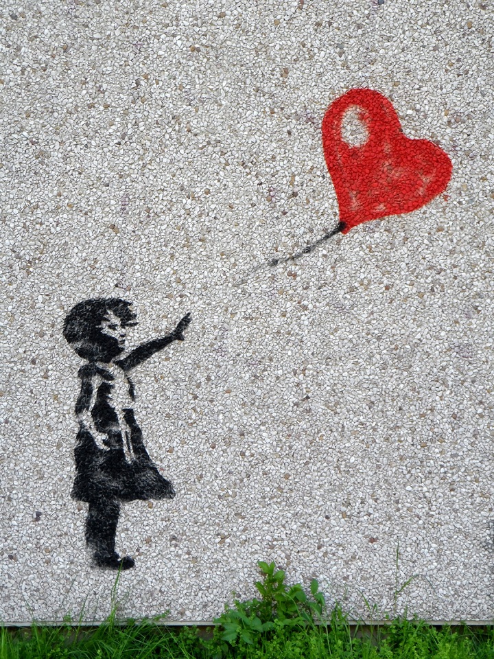 La imagen muestra un dibujo sobre una piedra de la silueta en negro de una niña intentando agarrar la cuerda de un globo de color rojo con forma de corazón.