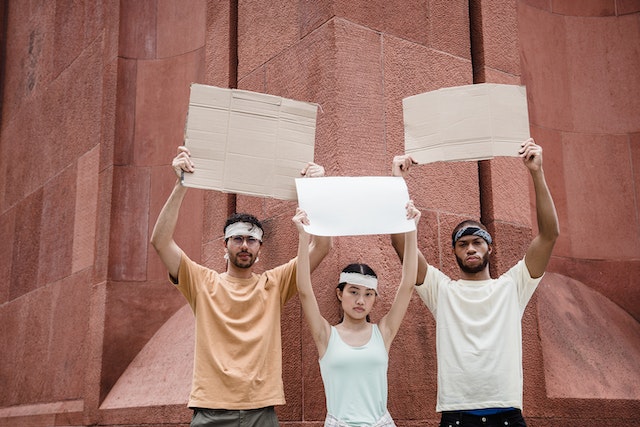 La imagen muestra tres personas con carteles en blanco levantados.