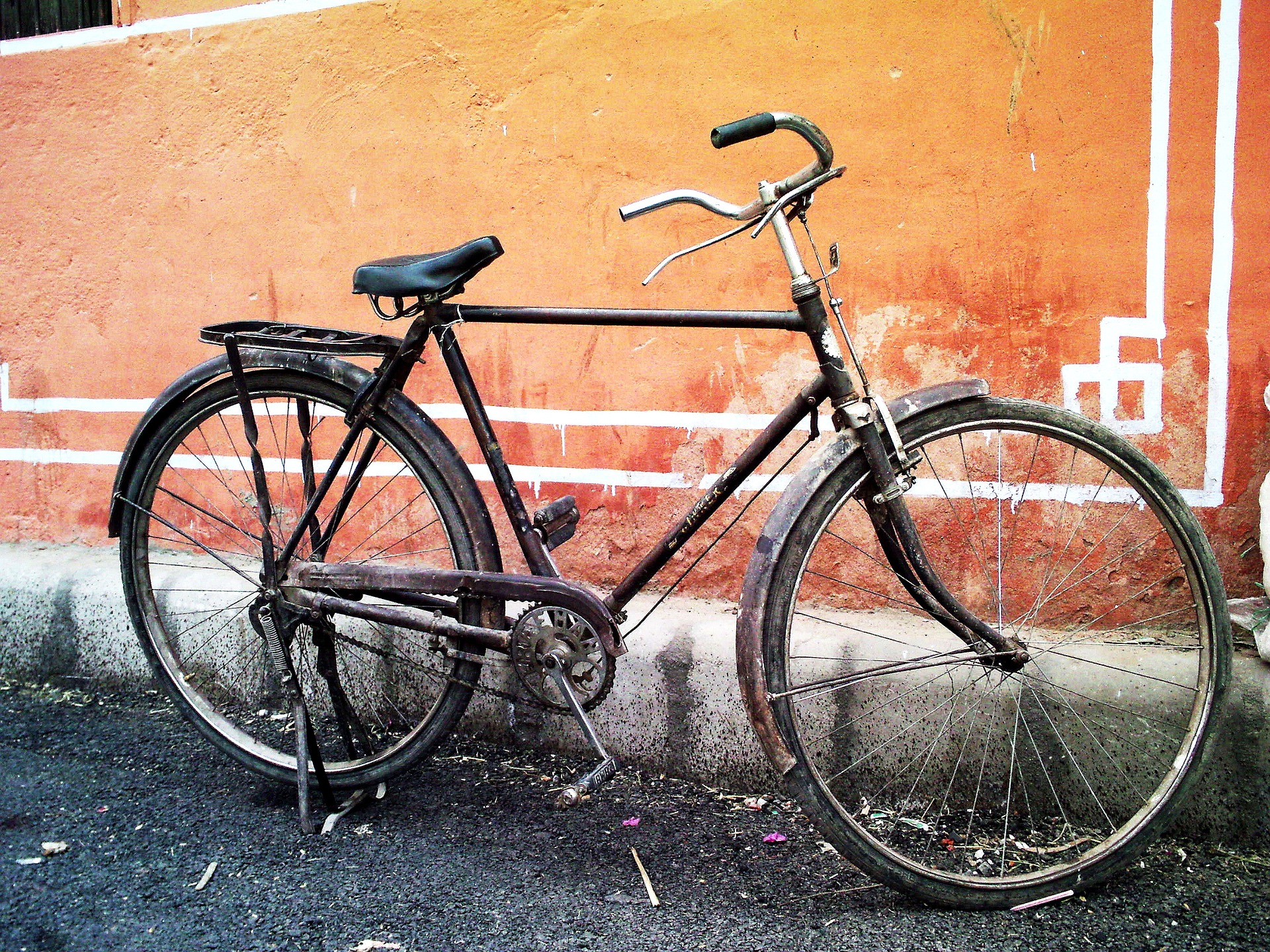 Imagen de bicicleta usada y deteriorada apoyada en el suelo cerca de la pared.