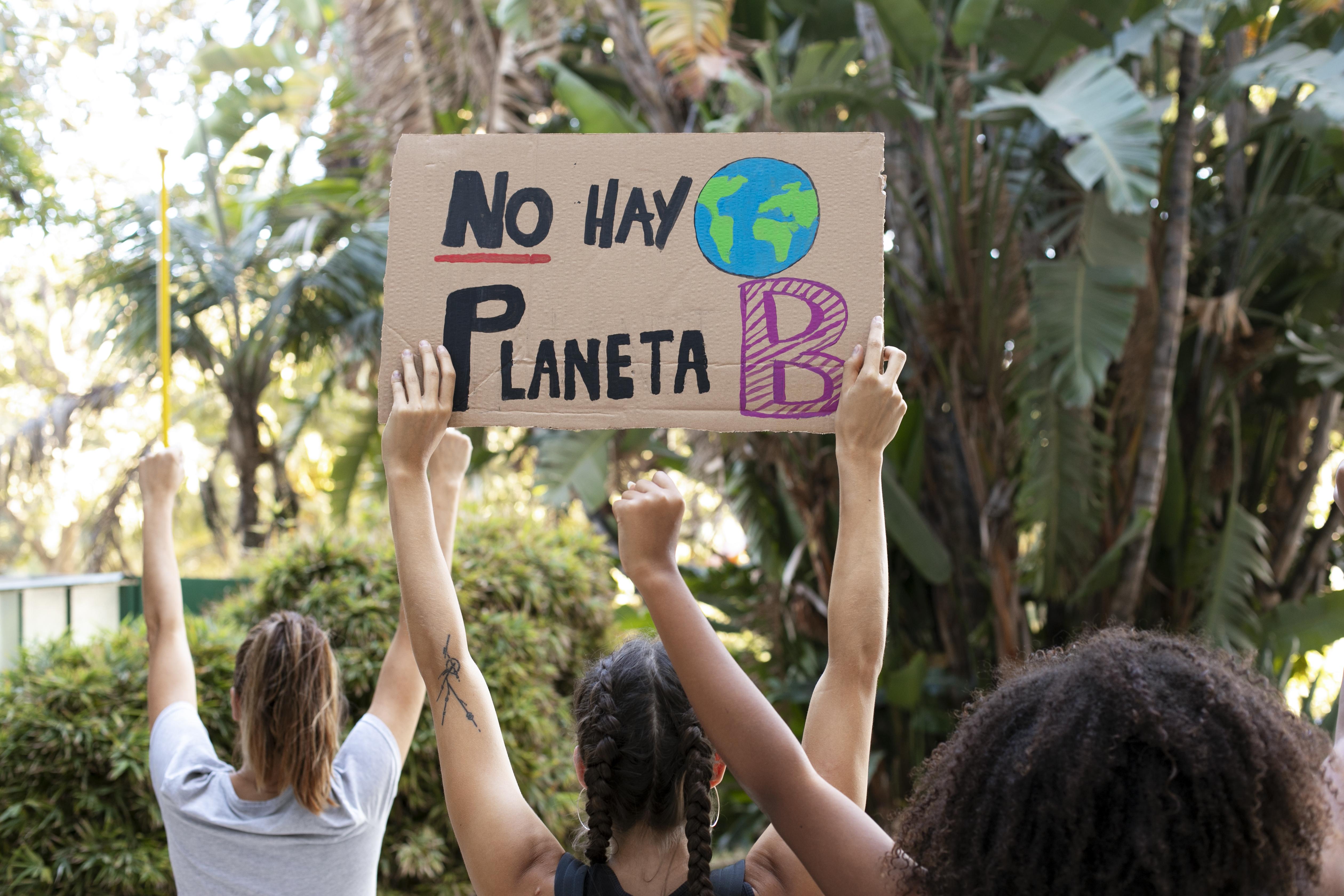 Chicas de espalda sujetando, con los brazos hacia arriba, un cartel que pone: “No hay planeta B”.