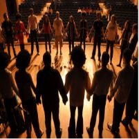 La imagen muestra un grupo de personas encima del escenario haciendo un círculo y dándose las manos.