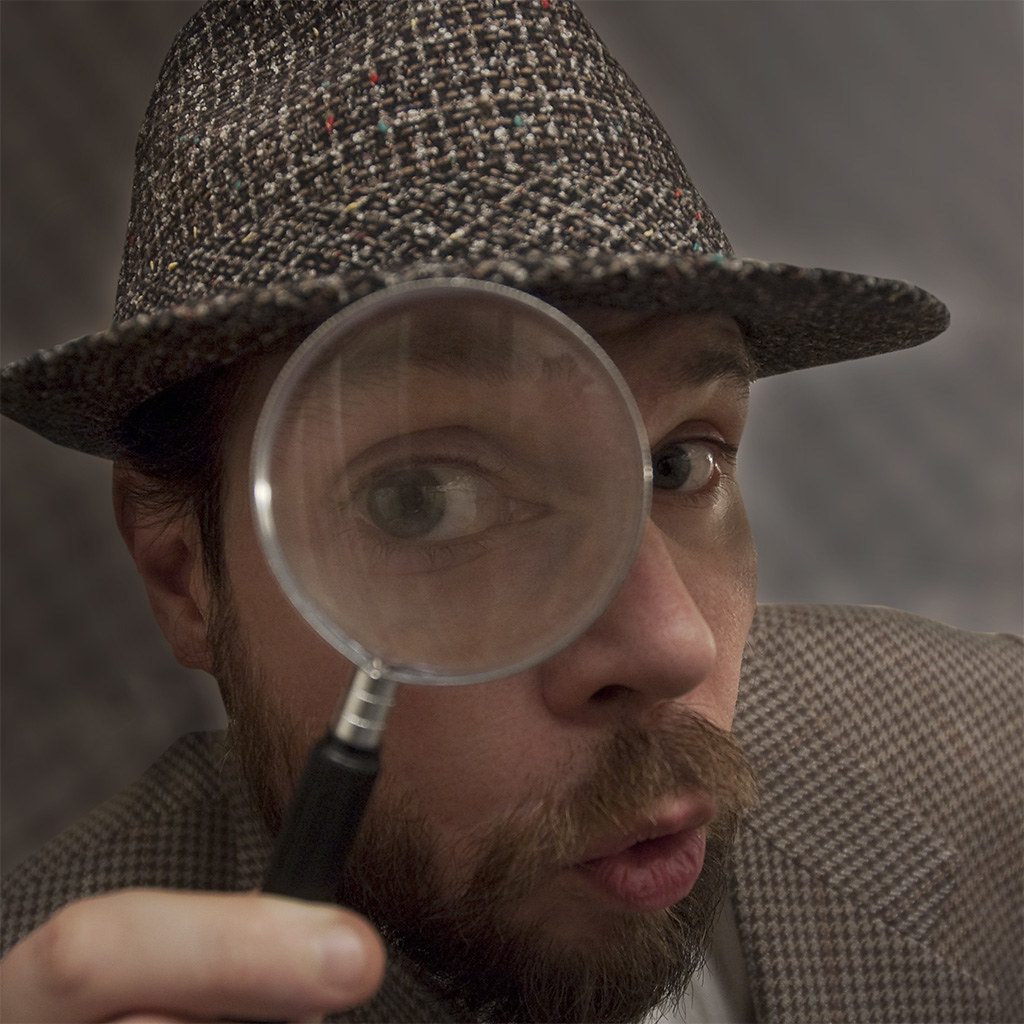 La imagen muestra un detective acercando una lupa a su ojo izquierdo.
