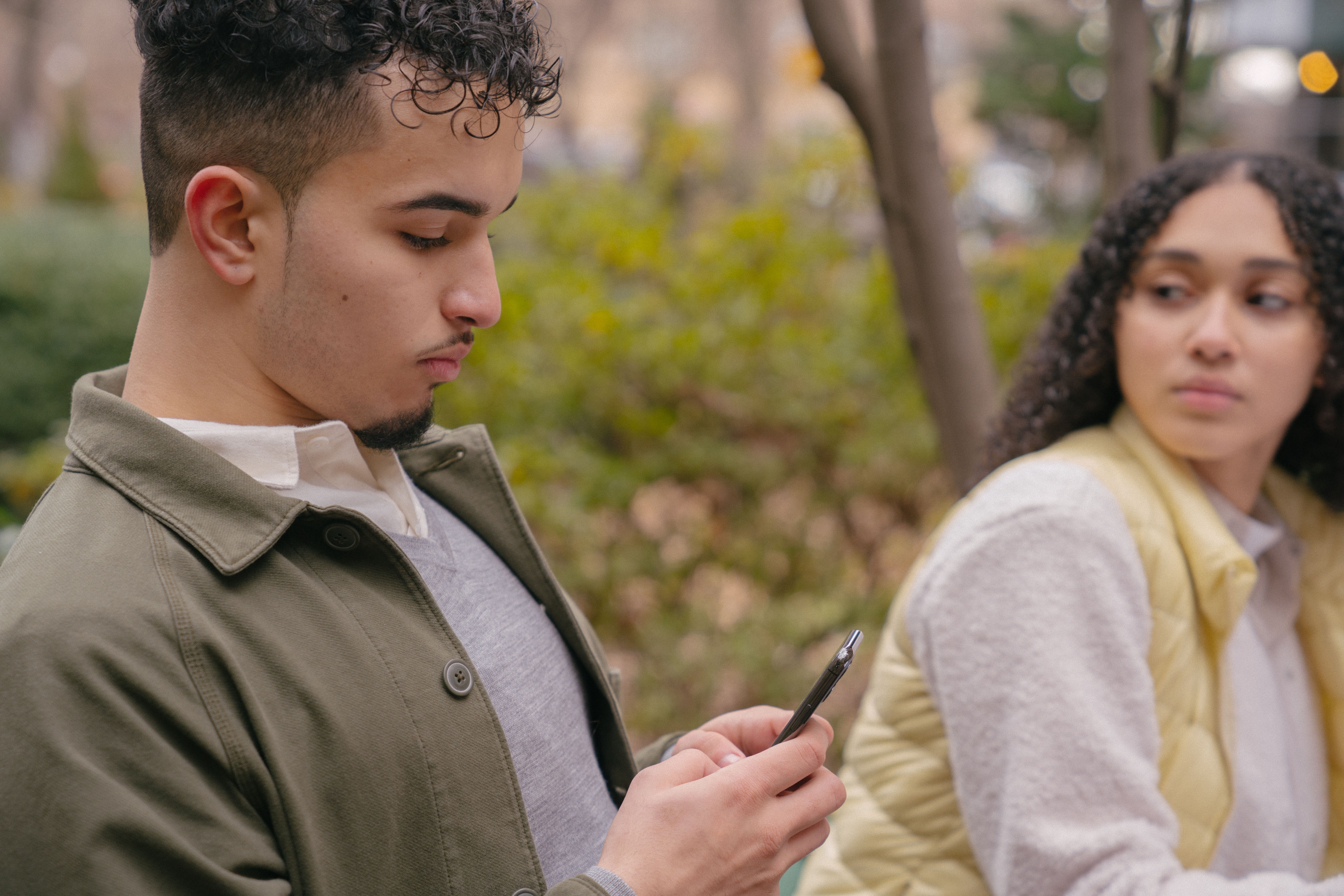 La imagen muestra a una pareja: un chico mirando el móvil y una chica, que parece enfadada, mirando al chico.