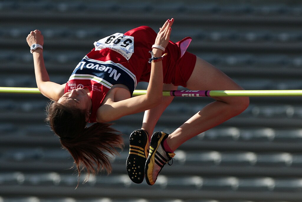 La imagen muestra una atleta superando un salto de altura.