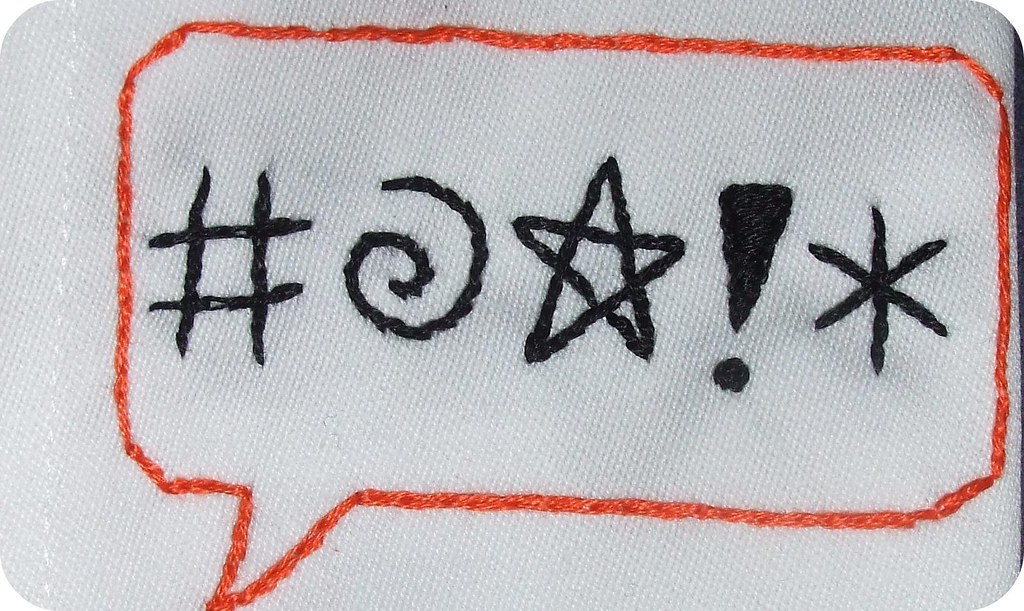 La imagen muestra un bocadillo de cómic con símbolos que dan a entender enfado bordado en una servilleta.