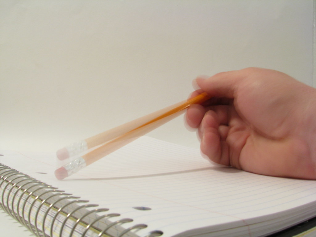 La imagen una mano sobre una libreta y el haz de un lápiz al golpearla con el extremo de la goma.