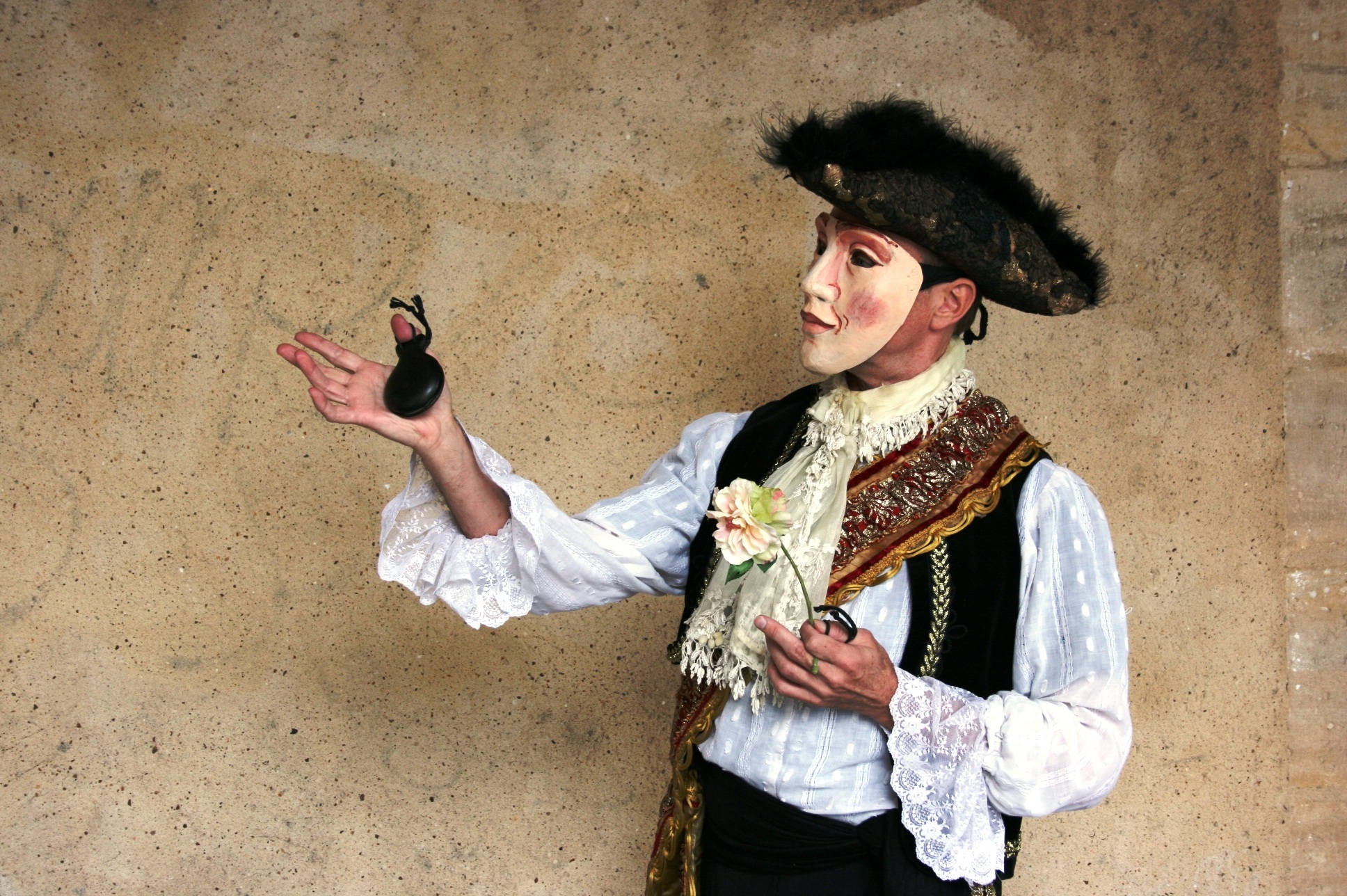 La imagen muestra a una persona dsifrazada con una careta sujetando en una mano una flor y en la otra una castañuela.