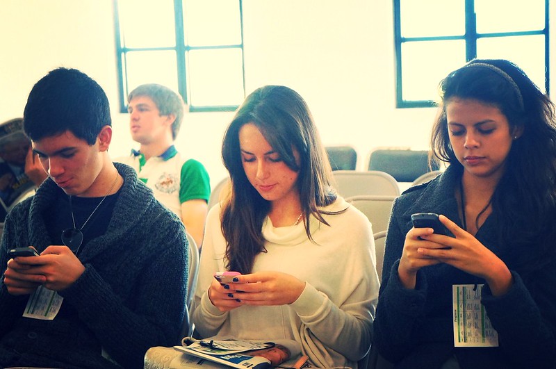 Tres chicos sentados miran atentamente sus móviles, olvidándose de sus compañeros.