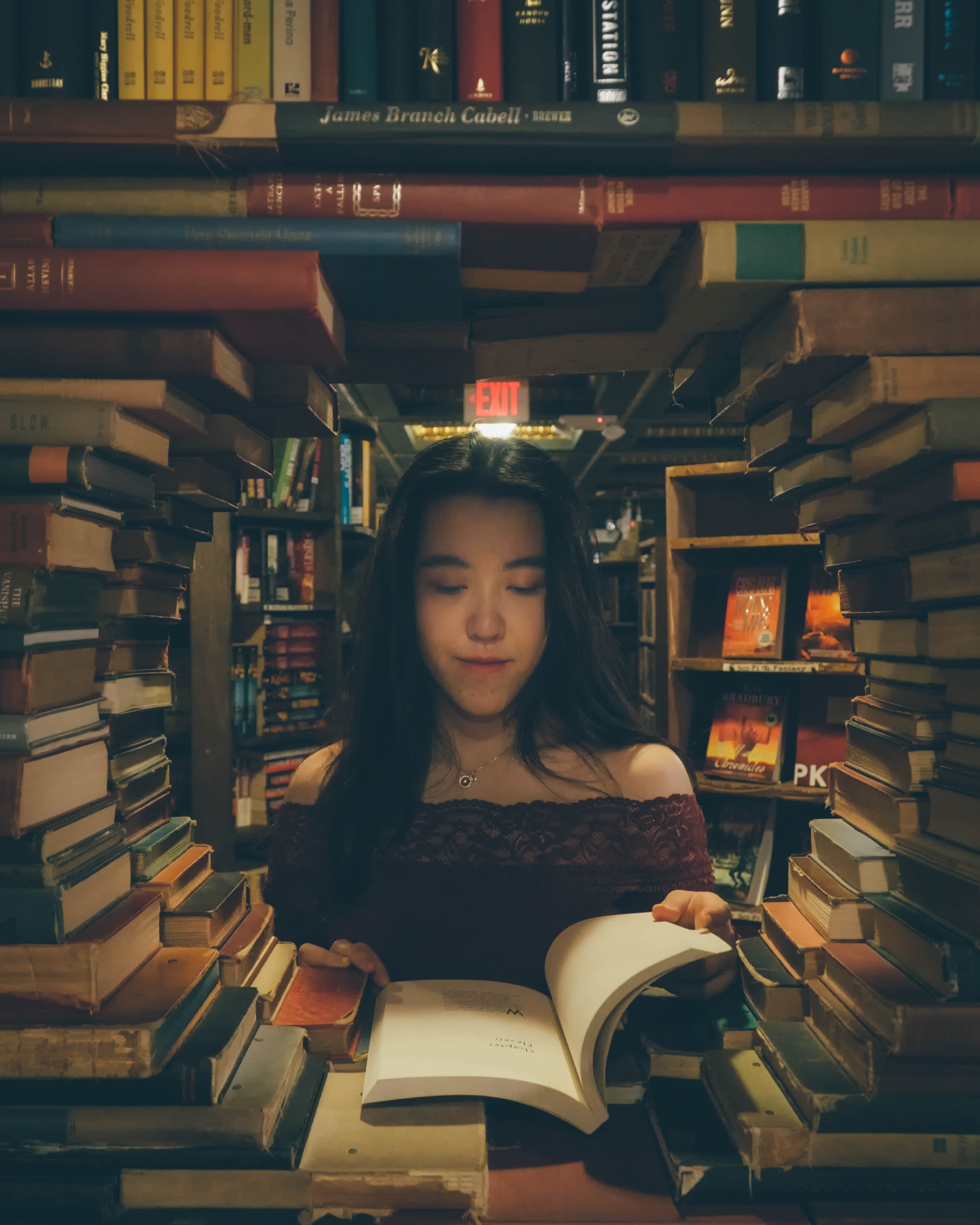 Una mujer rodeada de muchos libros en la biblioteca, lee uno de ellos.