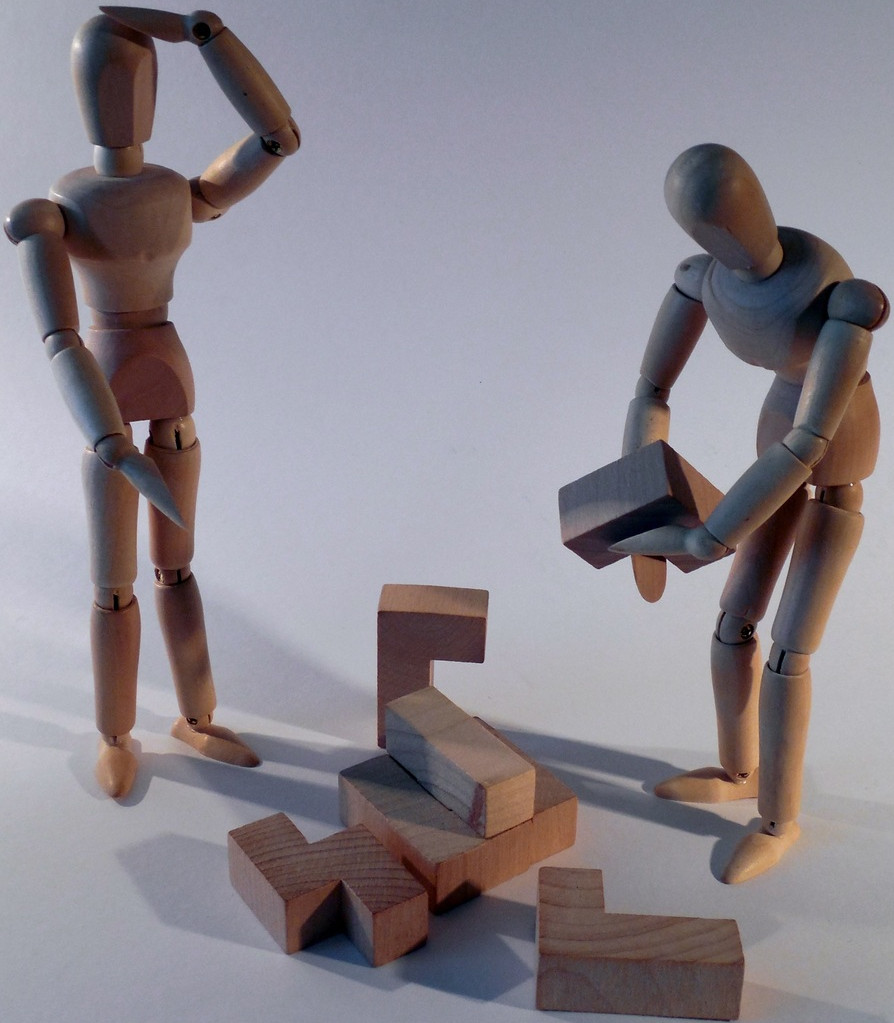 imagen de dos figuras humanas construidas con muñecos de madera tratando de trabajar en equipo para resolver un puzzle
