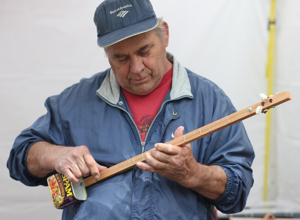 La imagen muestra a un señor de mediana edad tocando un instrumento fabricado con materiales reciclados.