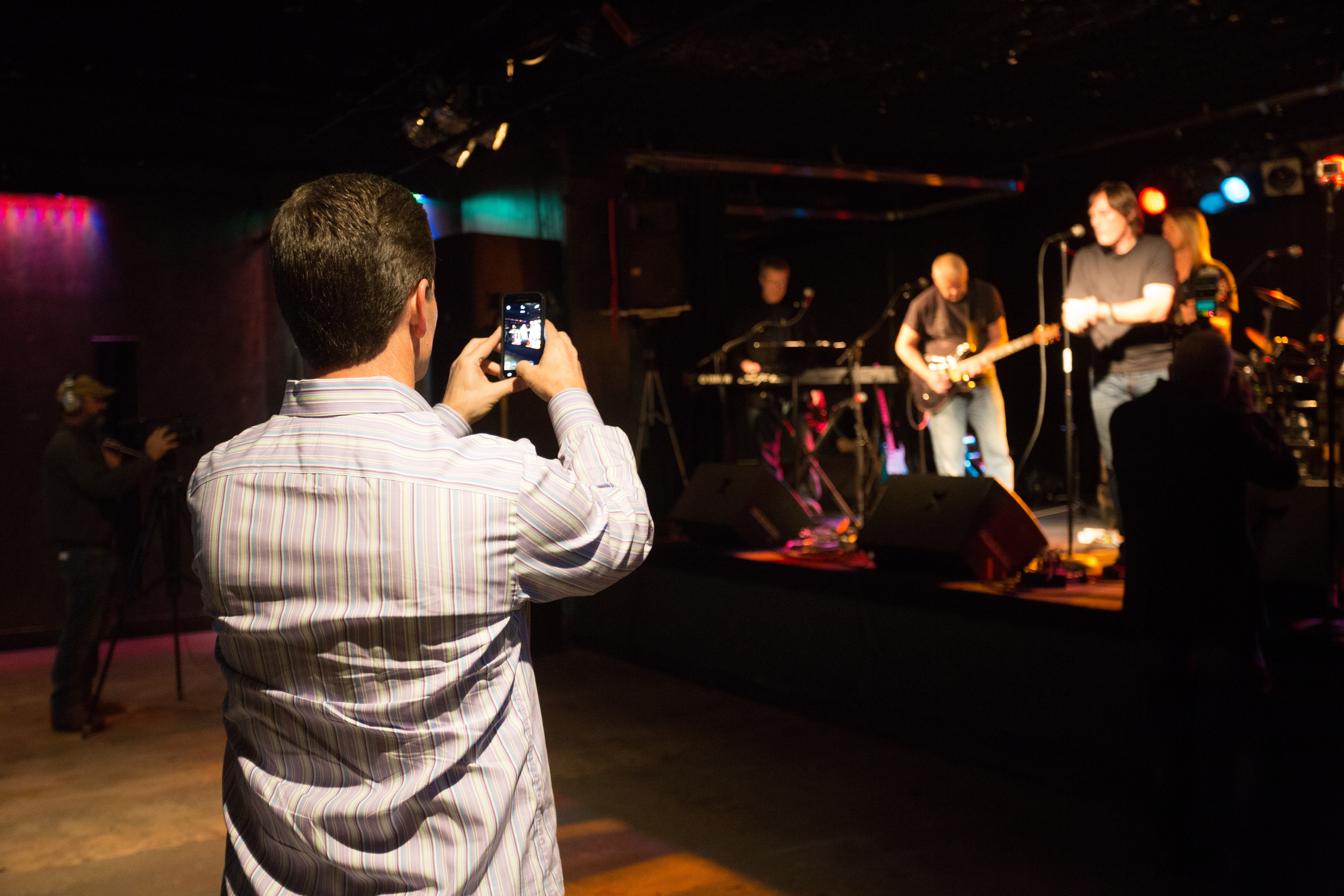 La imagen muestra a una persona grabando a un grupo de música