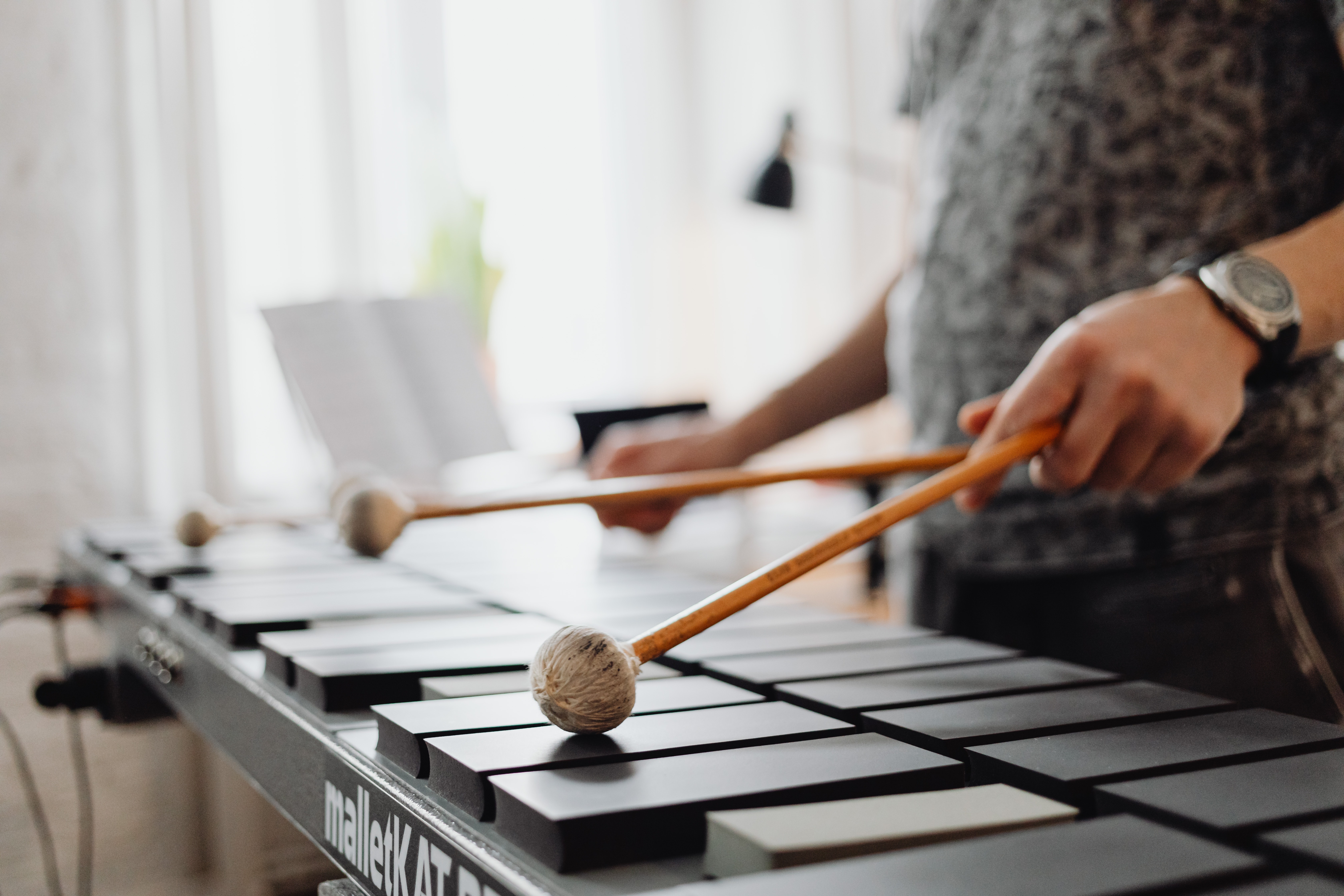 La imagen muestra unas manos con unas mazas tocando un instrumento de percusión.