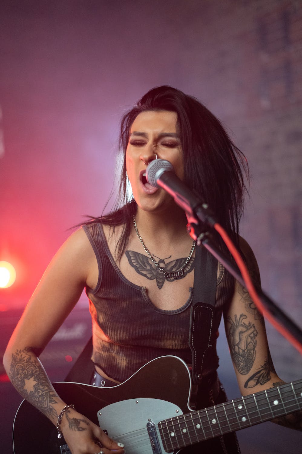 La imagen muestra chica con estilo rock cantando y tocando la guitarra