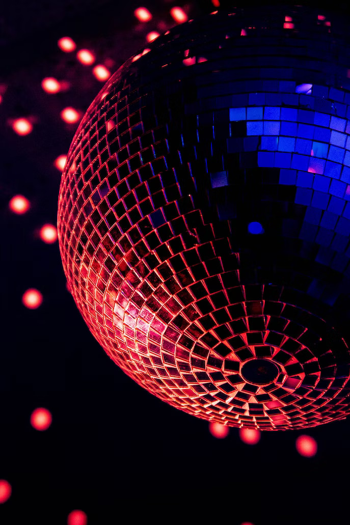 La imagen muestra bola de espejo de discoteca con fondo negro y reflejos en rojo