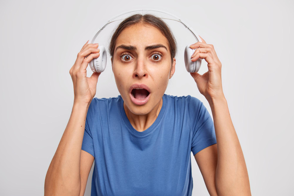 La imagen muestra una mujer sorprendida que se quita los auriculares y escucha algo con un sonido muy fuerte.