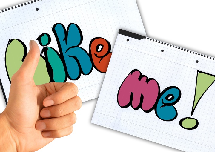  La imagen muestra una mano con el pulgar hacia arriba y dos hojas de cuaderno en las que aparecen las palabras en inglés “like” y “me”.
