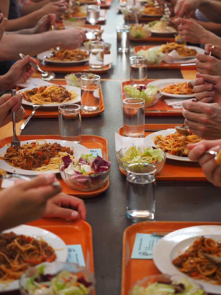 La imagen muestra bandejas en las mesas de un comedor escolar.