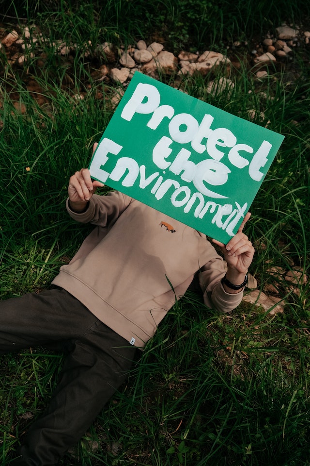 La imagen muestra un hombre tumbado con un cartel que pone “protejamos el medio ambiente”. 