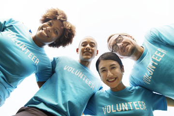 La imagen muestra cuatro jóvenes abrazados muy sonrientes con la misma camiseta en la que se lee la palabra “volunteer”.