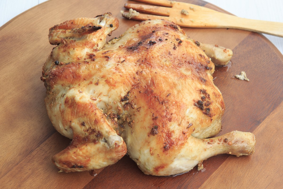 En la imagen se puede ver un pollo asado sobre una tabla de madera y preparado para trocear