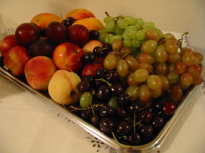 En la imagen se puede ver una bandeja plateada llena de fruta variada, tales como uvas, cerezas, melocotones, ciruelas y mangos