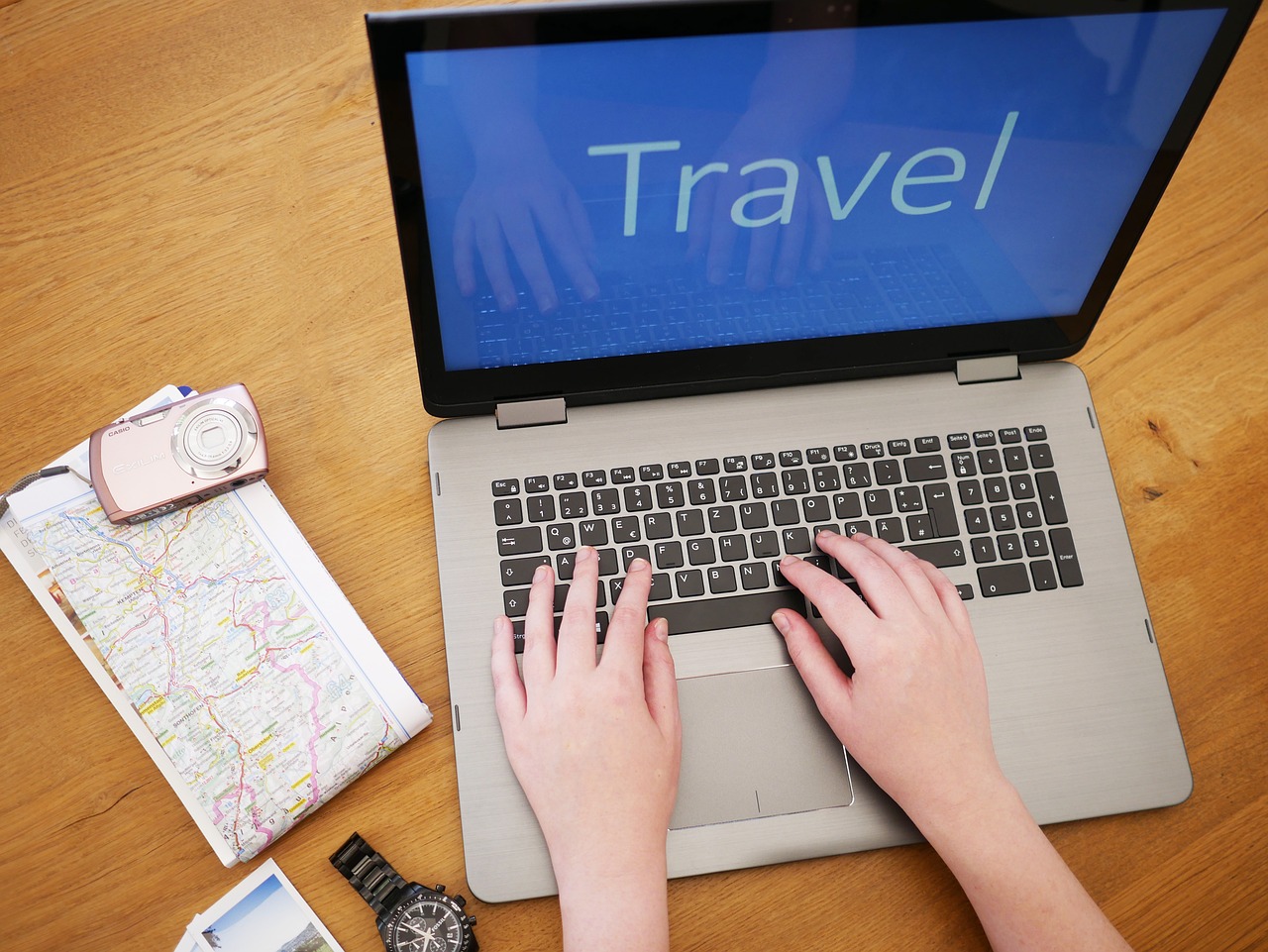 La imagen muestra un ordenador con la palabra travel, un mapa y una cámara de fotos.