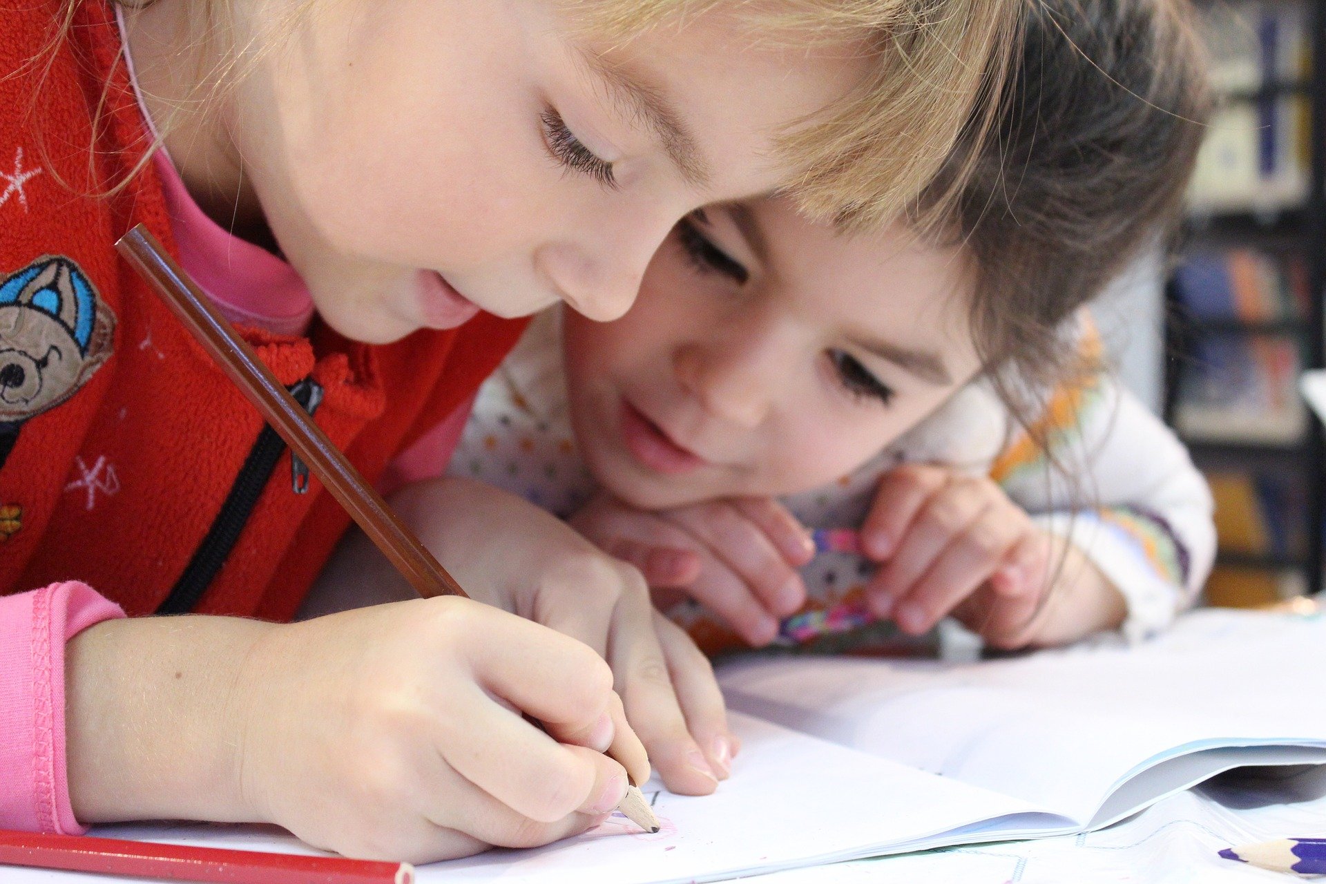 Dos niños sentados juntos escriben en un cuaderno.