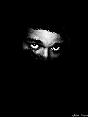 En una imagen negra se ve un trozo de un rostro, se ve parte de la frente, los ojos y cejas y la nariz. Lo que se ve está en blanco y negro.