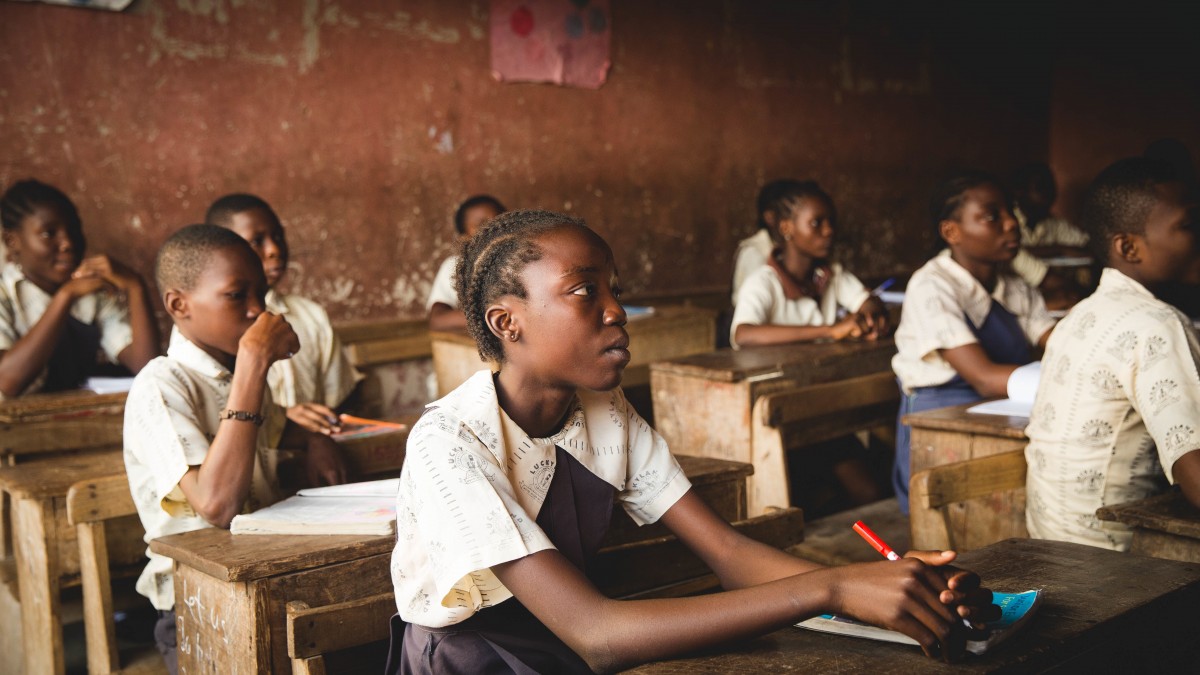 Imagen de un aula de una escuela africana. Se ven varios chicos y chicas de raza negra sentados en sus pupitres.