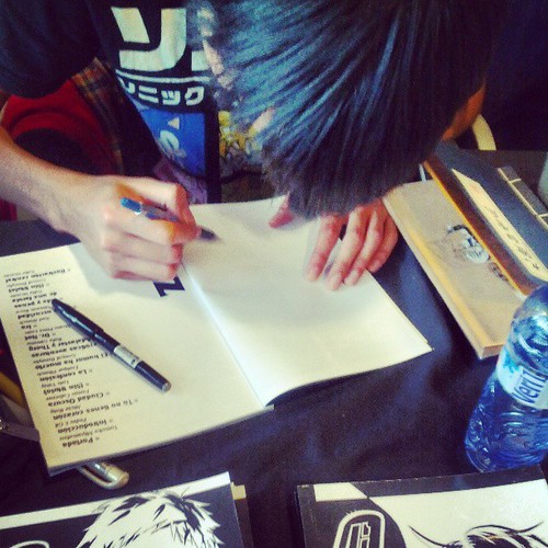 Foto desde arriba de un chico dibujando con un lápiz y un bolígrafo negro, en un cuaderno.