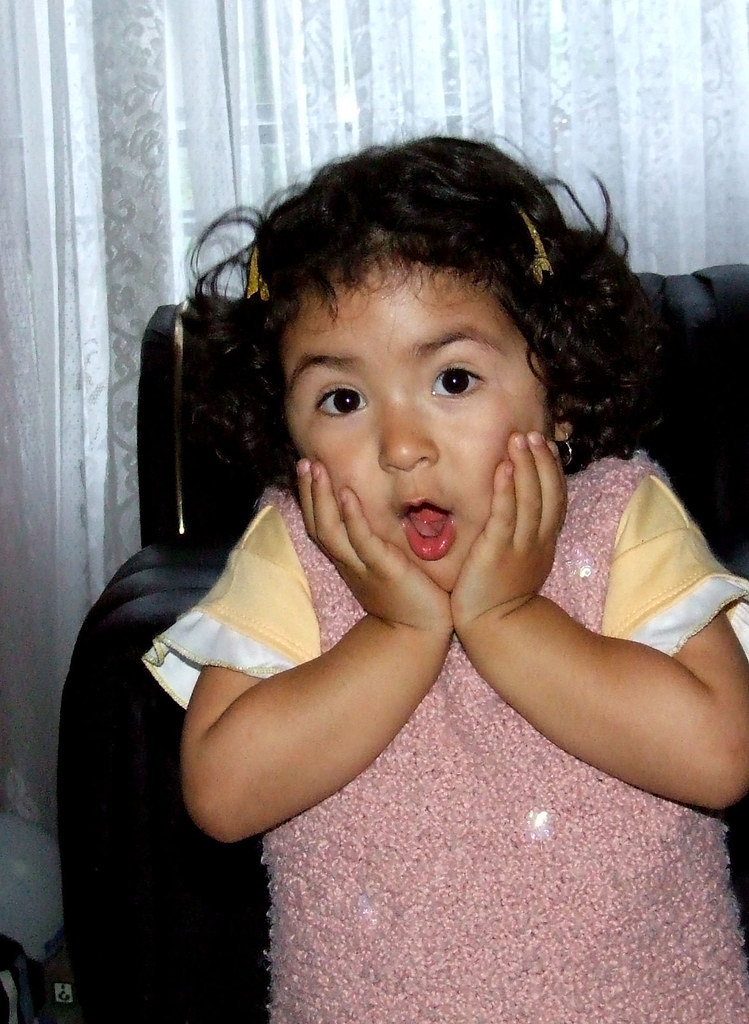Imagen de una niña pequeña, con el pelo negro recogido en dos coletas, que se muestra sorprendida. Tiene las dos maños sobre sus dos mejillas y la boca con forma de o.